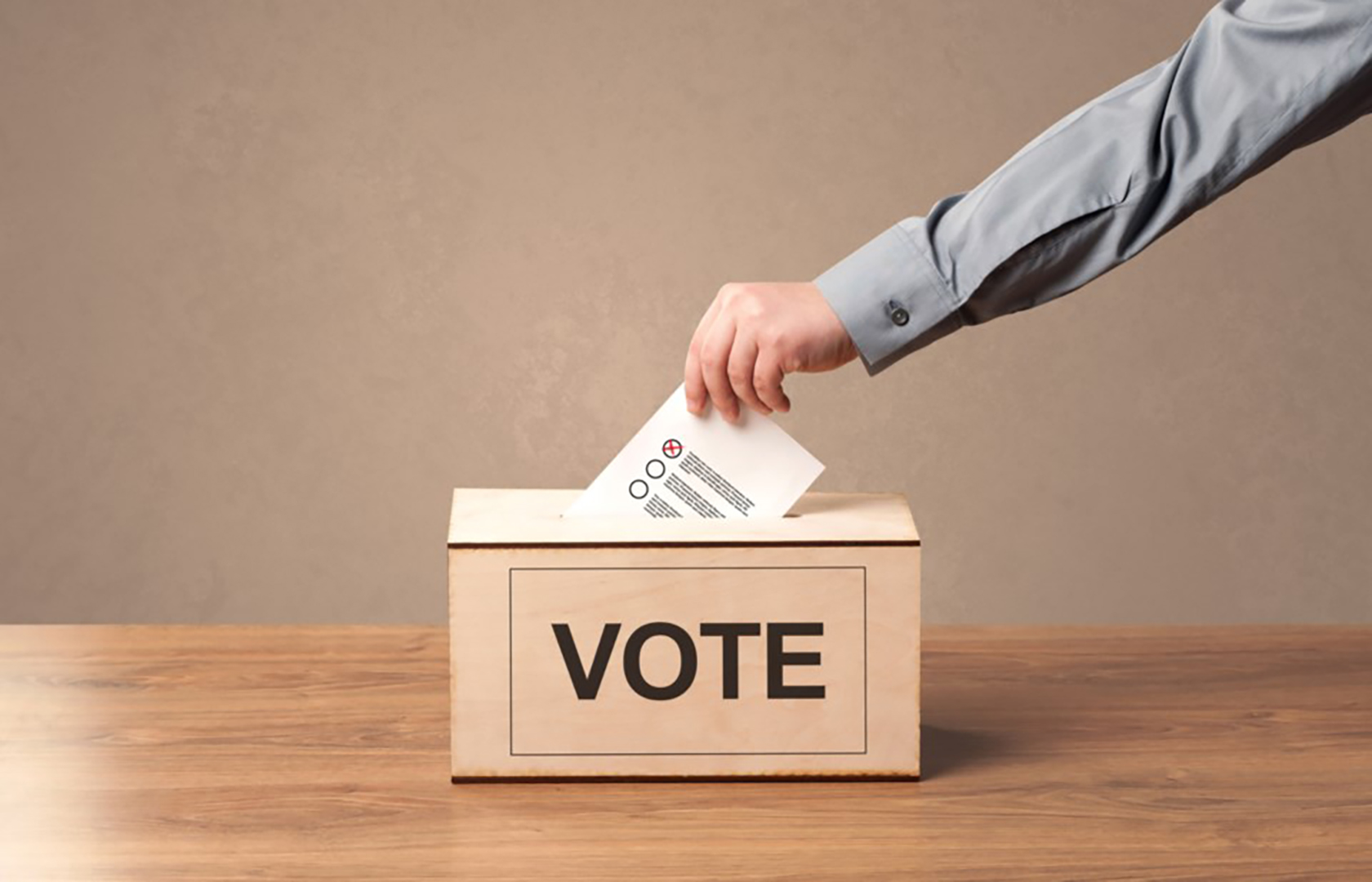 A hand places a ballot in a voting box